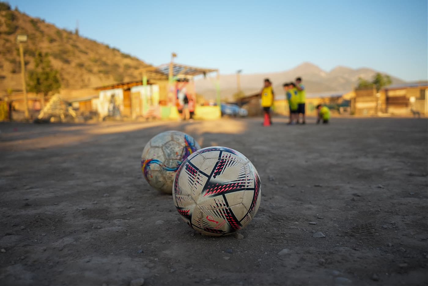 Dos balones apoyados en la tierra de la cancha con el cerro de fondo