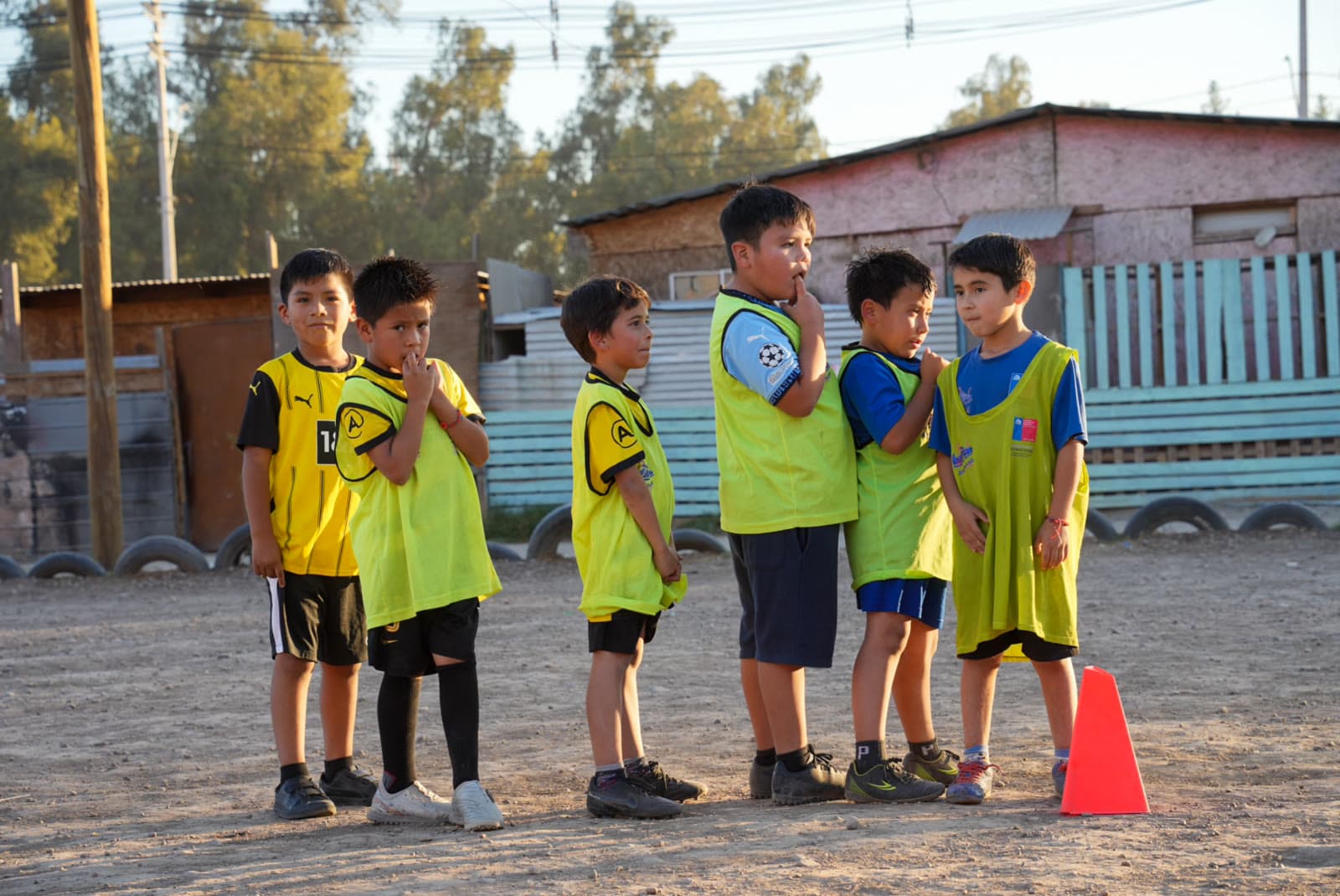 Grupo de niños con petos del equipo conversando antes de entrenar, frente a las casas del barrio