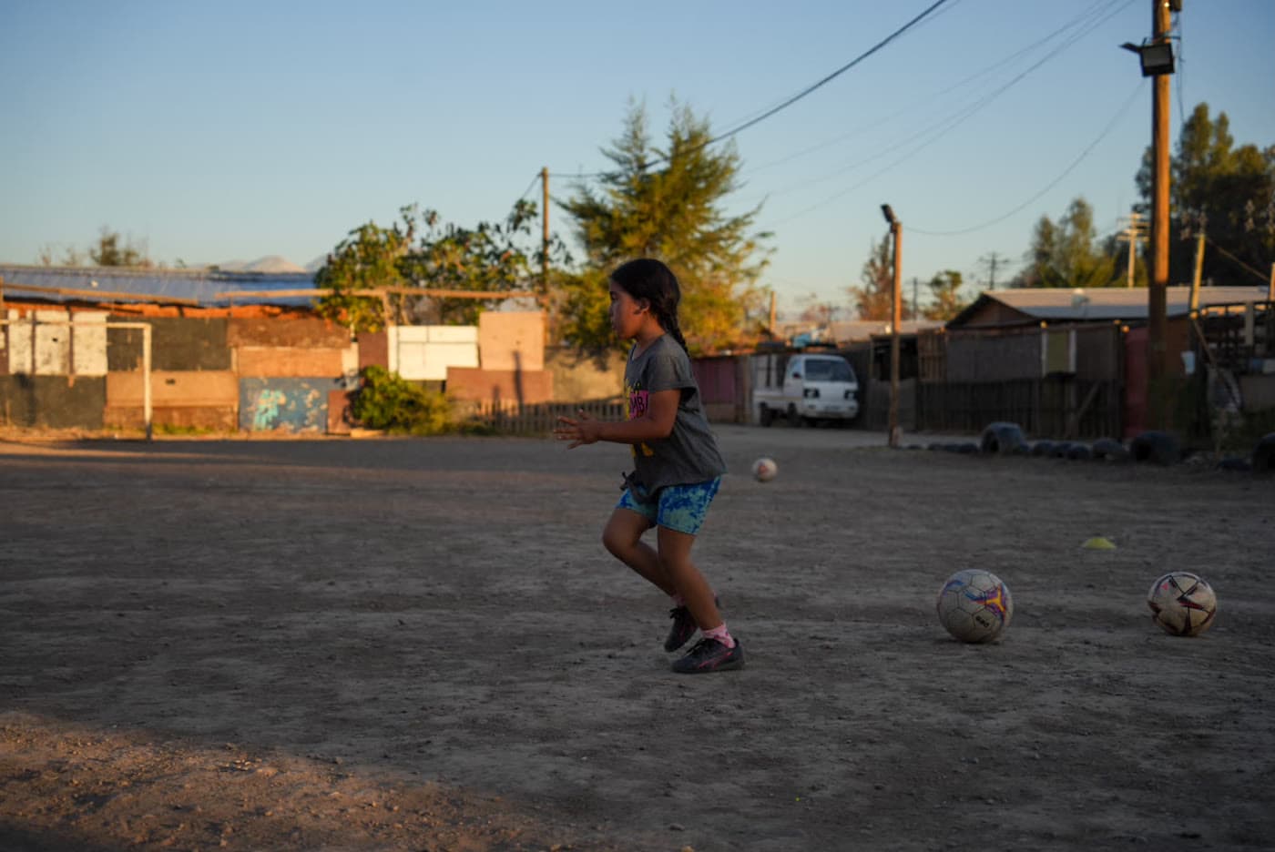 Una niña conduce el balón en la cancha de tierra del barrio