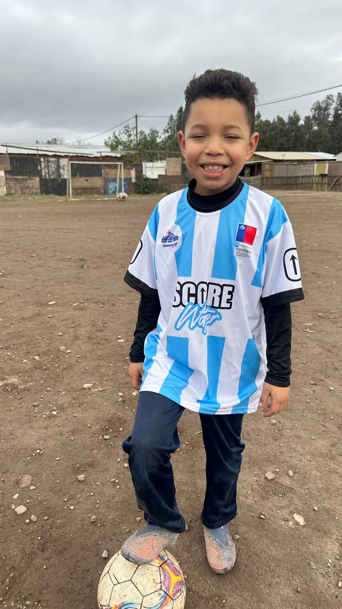 Niño sonriendo con la camiseta del equipo y el pie sobre el balón